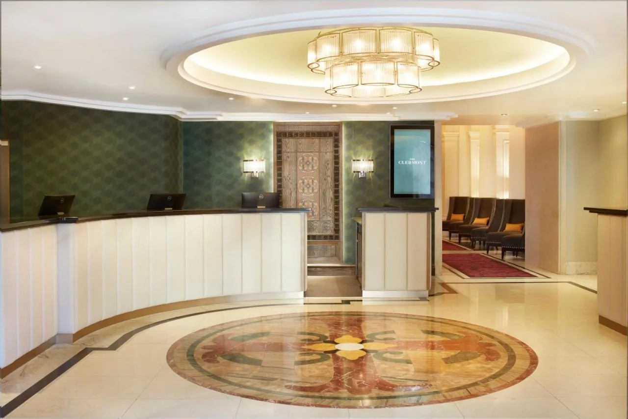 a hotel lobby with a reception desk and a chandelier at The Clermont London, Charing Cross in London